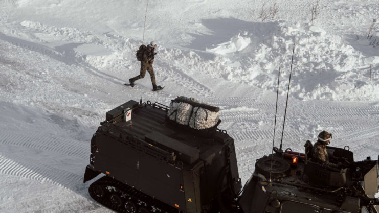 UK Royal Marine running in the snow, alongside two tanks