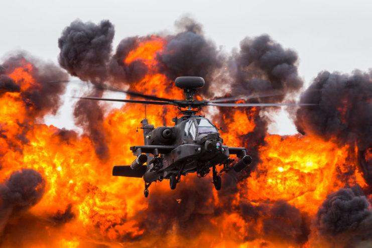 WAH-64D Apache helicopter flying in front of a wall of fire