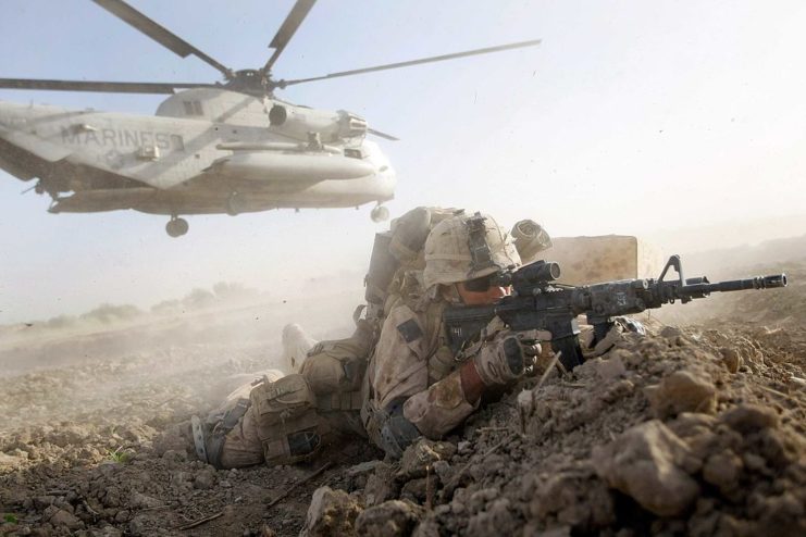 US Marine aiming a firearm while a military helicopter hovers behind him