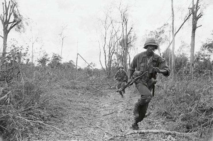 Soldiers with the 1st Infantry Division running through tall grass