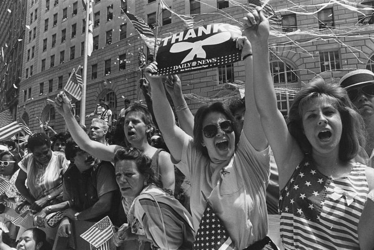 Parade attendees hold up American flags and signs