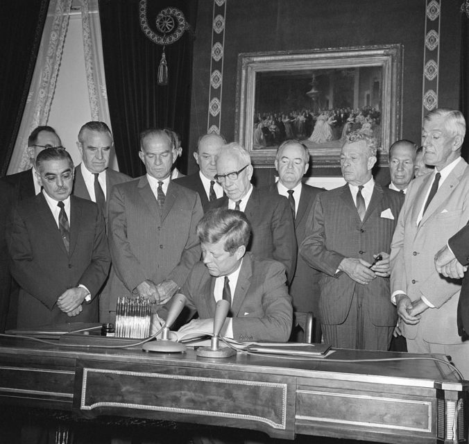 President John F Kennedy signs the Nuclear Test Ban Treaty surrounded by other US officials 
