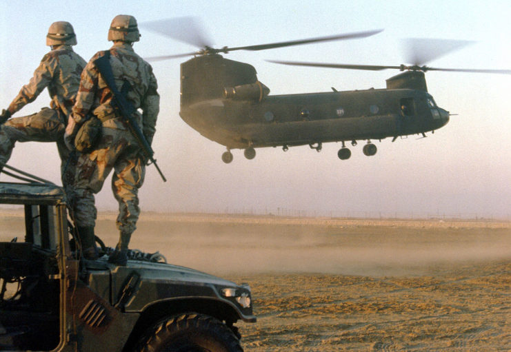 Two soldiers with the 82nd Airborne Division watching a CH-47 Chinook helicopter landing
