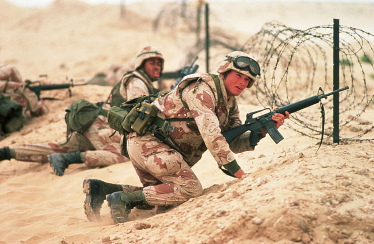 Two US Marines crouched down behind a barbed wire fence