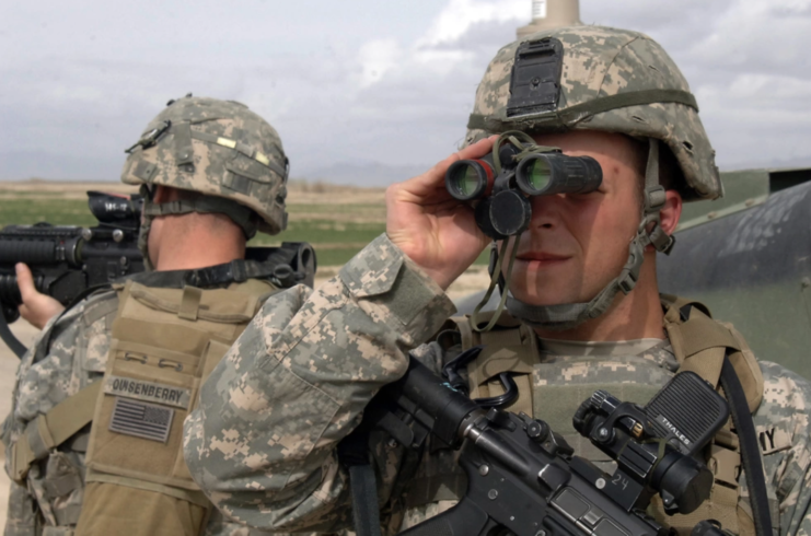 Sgt. Joseph Evans looking through binoculars while Spc. Brendon Quisenberry stands watch while armed