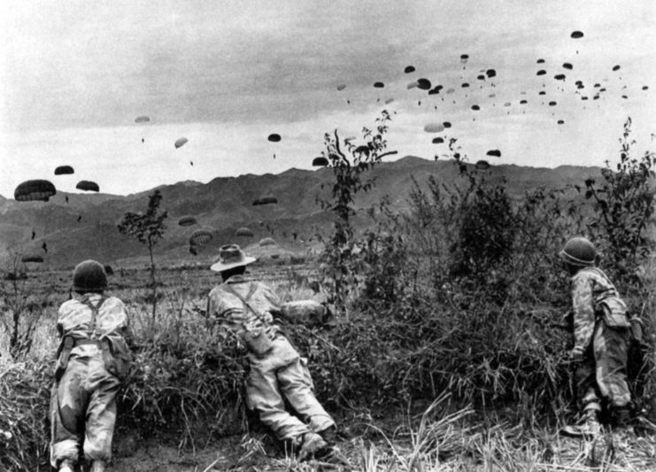 Three soldiers watching as paratroopers parachute to the ground
