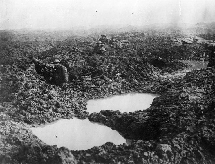 Soldiers with the 16th Canadian Machine Gun Company laying low in shell holes on a muddy battlefield