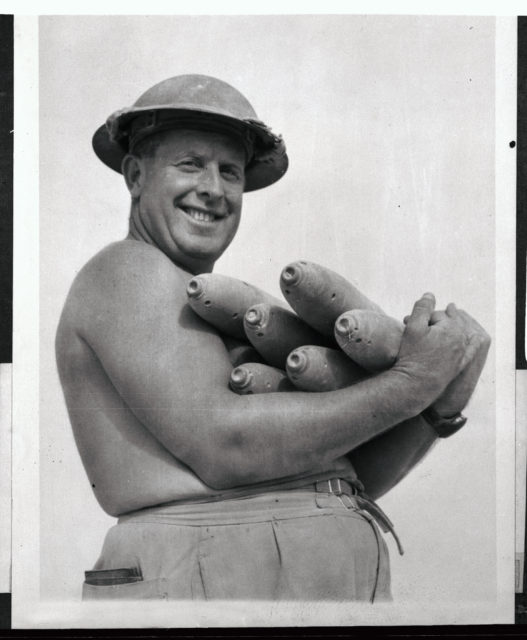 Shirtless Australian soldier carrying 75 mm shells