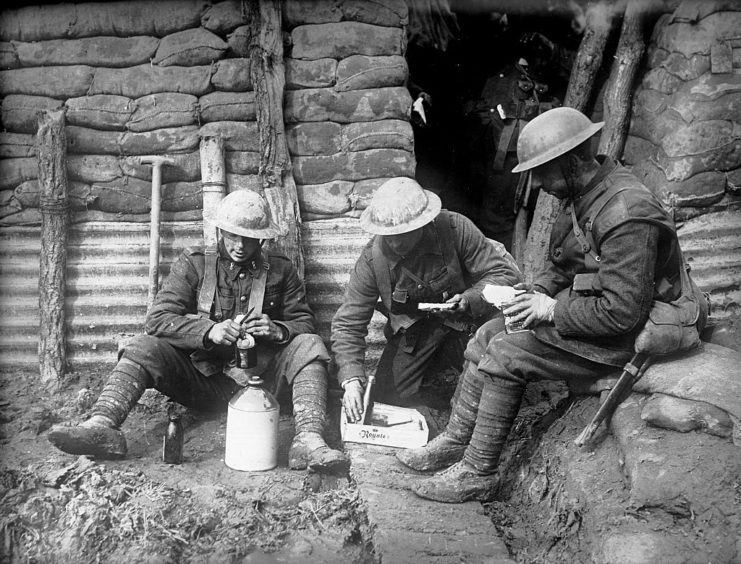 Three Canadian soldiers sitting in a trench