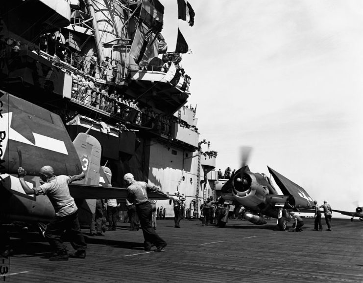 Crewmen standing around two Grumman F6F Hellcats on the flight deck of the USS Essex (CV-9)