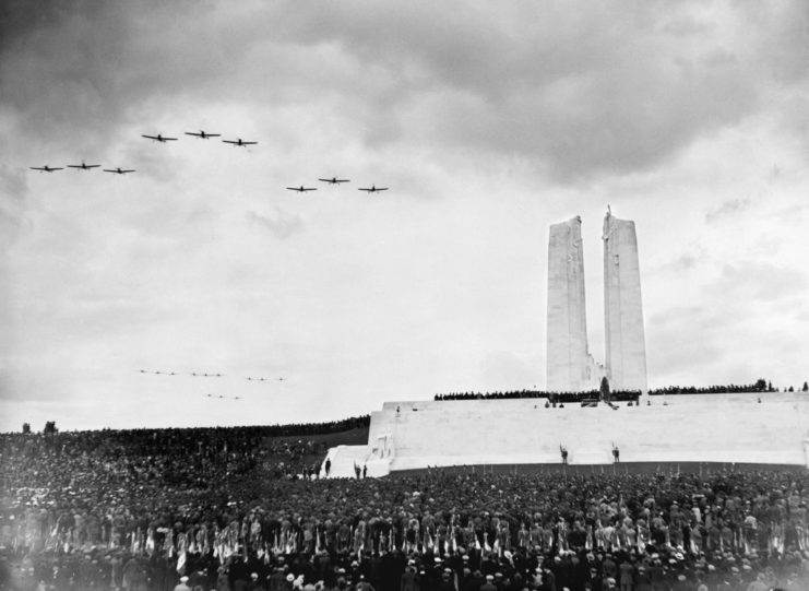 Vimy Ridge Memorial, with a crowd gathered before it and aircraft flying overhead