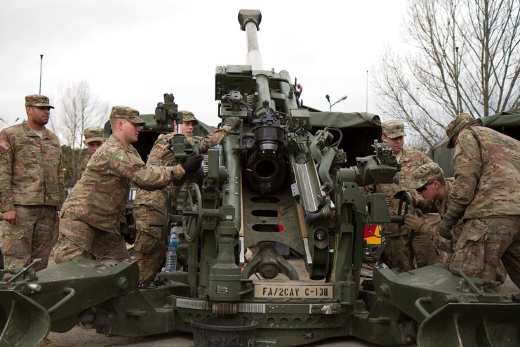 US Army soldiers standing toward the rear of an M777 howitzer