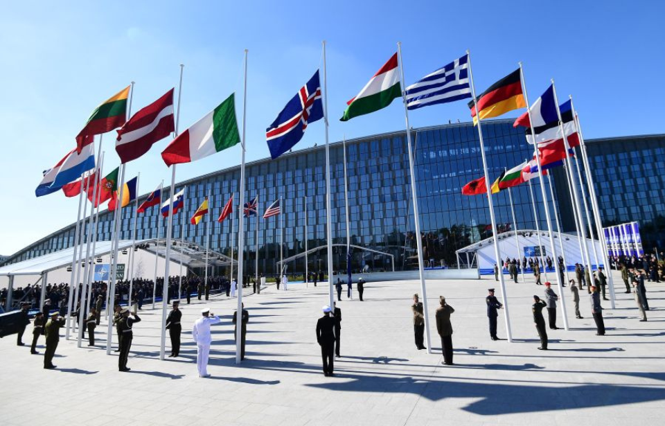 Military personnel standing beneath the flags at the front of NATO's headquarters