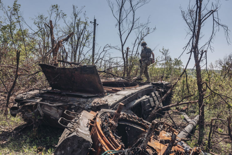 Ukrainian soldier standing on top of a destroyed Russian tank