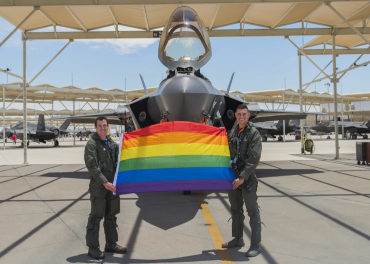 Maj. Tyler McBride and Capt. Justin Lennon holding a Pride flag in front of an aircraft
