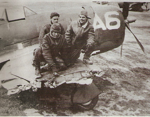Three men sitting atop a damaged Republic P-47 Thunderbolt wing