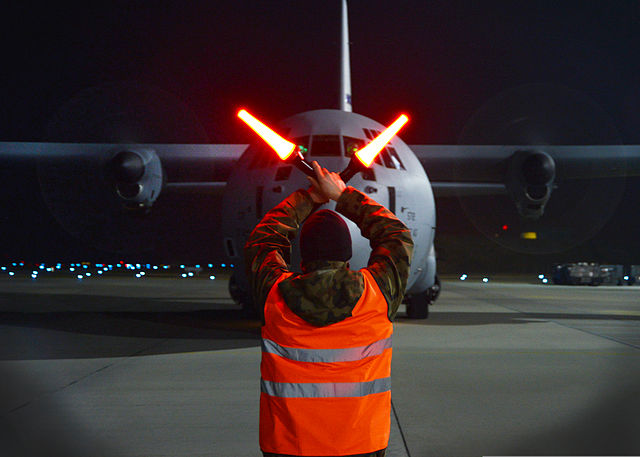 Man directing a Lockheed C-130 Hercules down the runway
