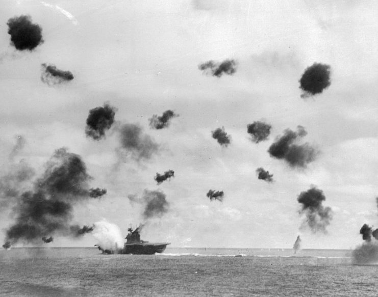 USS Yorktown (CV-5) at sea while anti-aircraft shells explode in the air