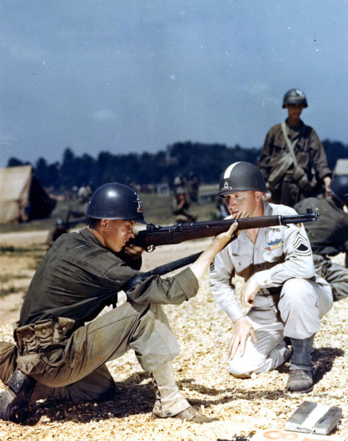 Recruit watching as a sergeant aims an M1 Garand while in a kneeling position