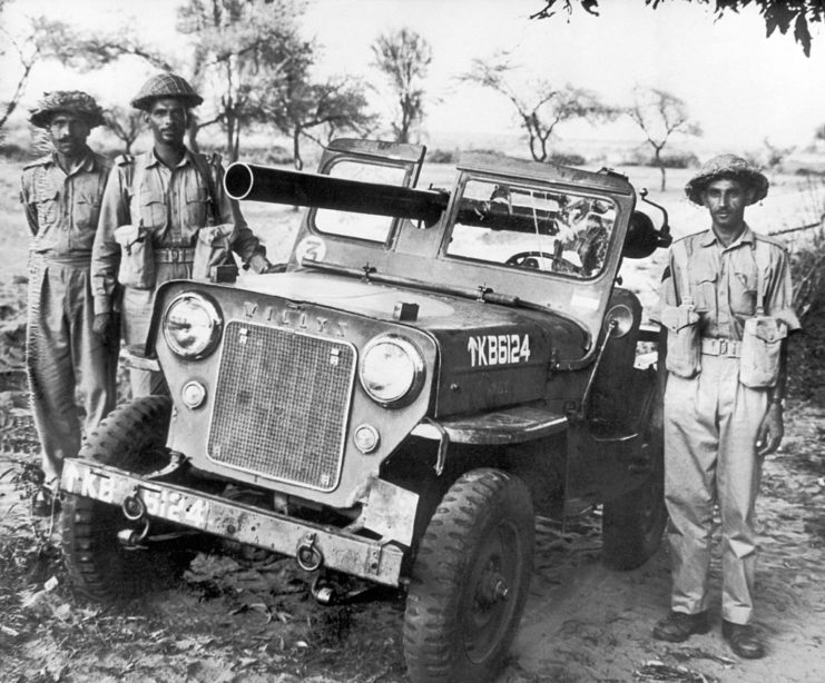 Three Indian soldiers standing next to a Jeep equipped with an anti-tank gun