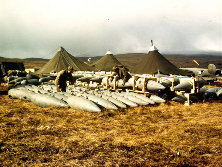 Two crewmen standing among drop fuel tanks