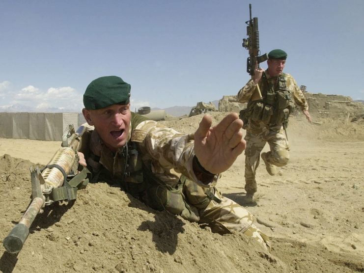 British Royal Marine Commando holding his hand out, as another runs forward while holding his firearm
