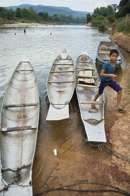 Little boy partially standing inside a canoe made from fuel tanks