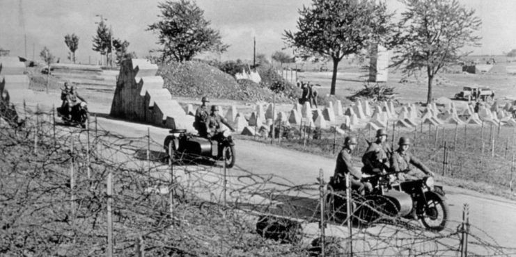 Soldiers driving motorcycles through the boundaries of the Siegfried Line