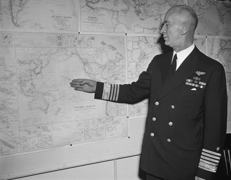 Ernest King pointing to a map pinned to a wall