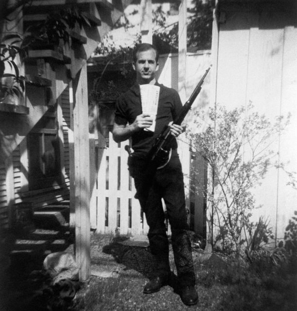 Lee Harvey Oswald holding his Carcano and a newspaper in his backyard