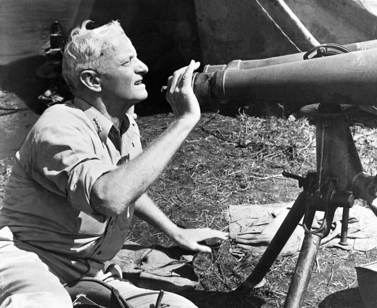 Chester Nimitz kneeling behind a set of large binoculars