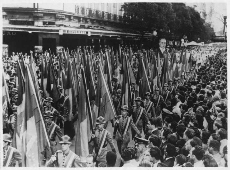 Brazilian soldiers parading down a street while carrying the country's flag