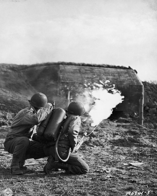 Two US troops crouching while they fire their flamethrowers