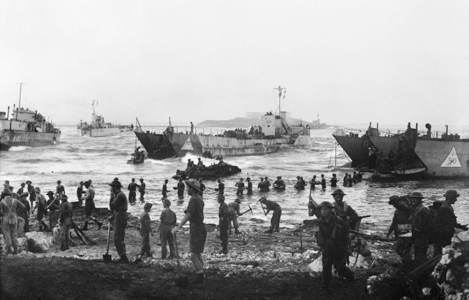 Soldiers watching while additional troops disembark from a landing craft