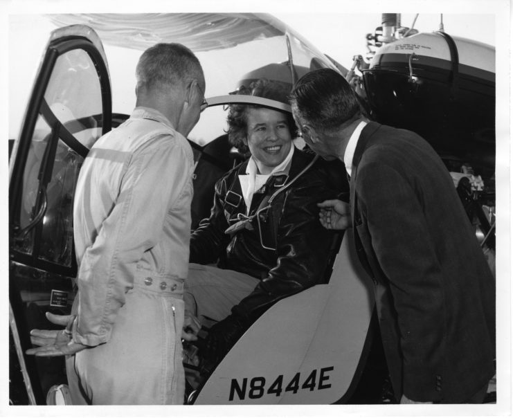 Dora Dougherty Strother sitting in the cockpit of a helicopter while speaking with two men
