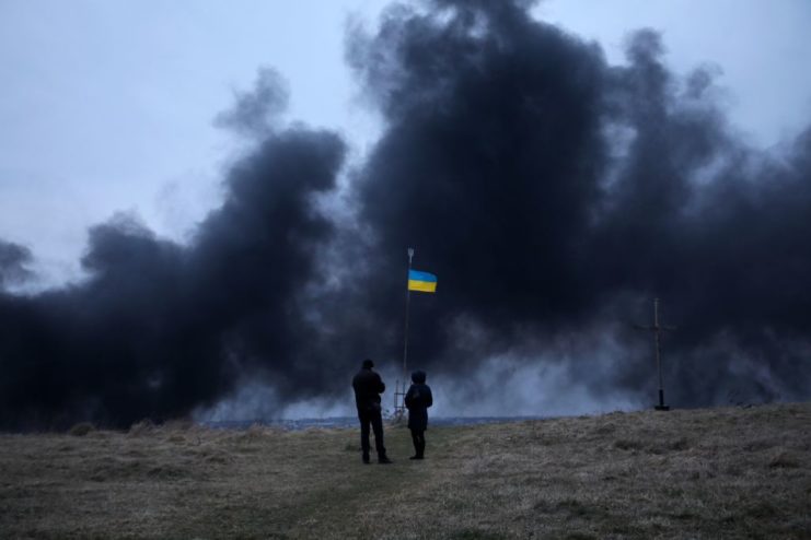 Smoke billowing around two people and the Ukrainian flag