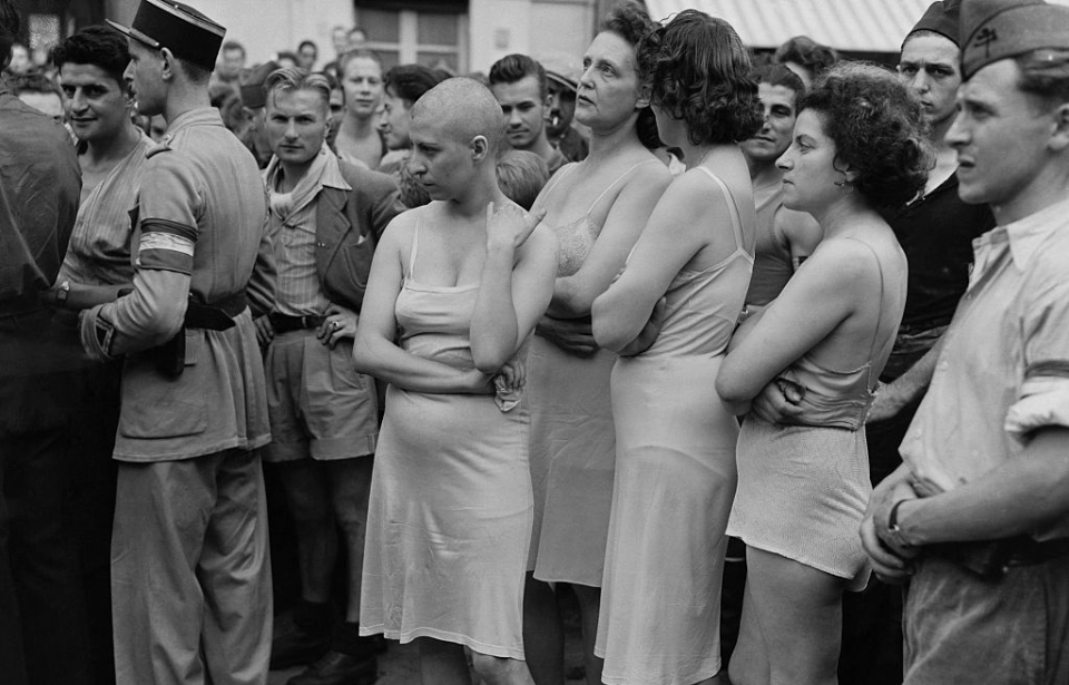 Three women, one with her head shaved, standing in a crowd