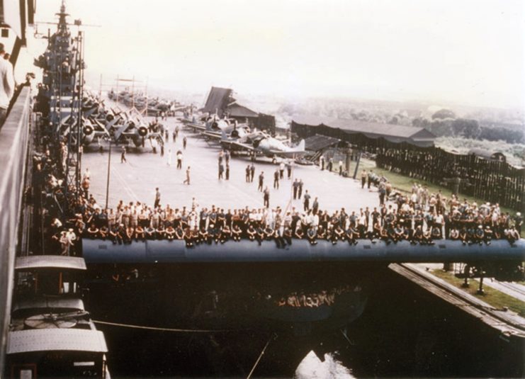 The USS Yorktown travels through the Panama Canal with people sitting on one of the guns