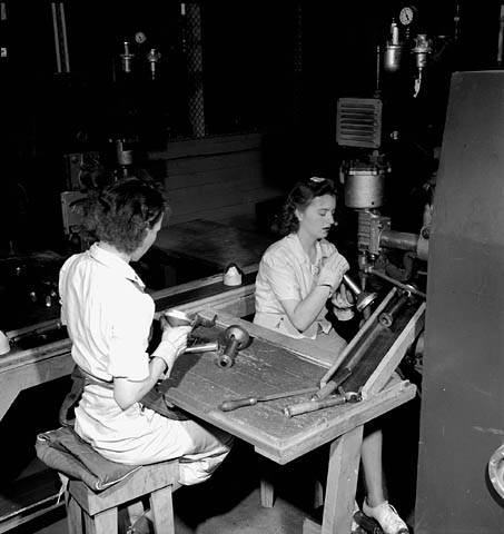 Two women sitting at a table while working on parts for the PIAT