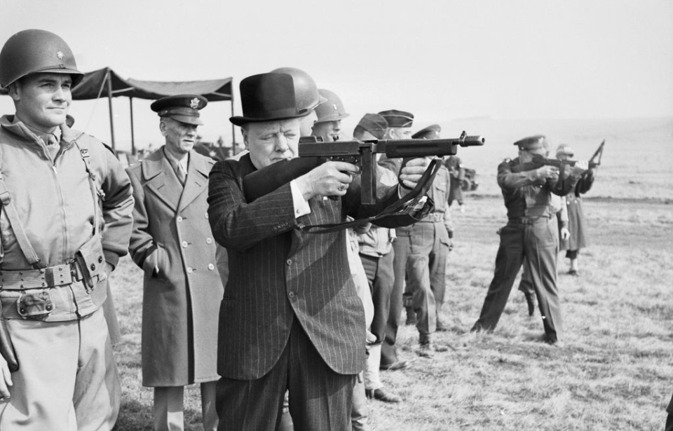 Winston Churchill aiming a Thompson "Tommy Gun" while standing with American soldiers