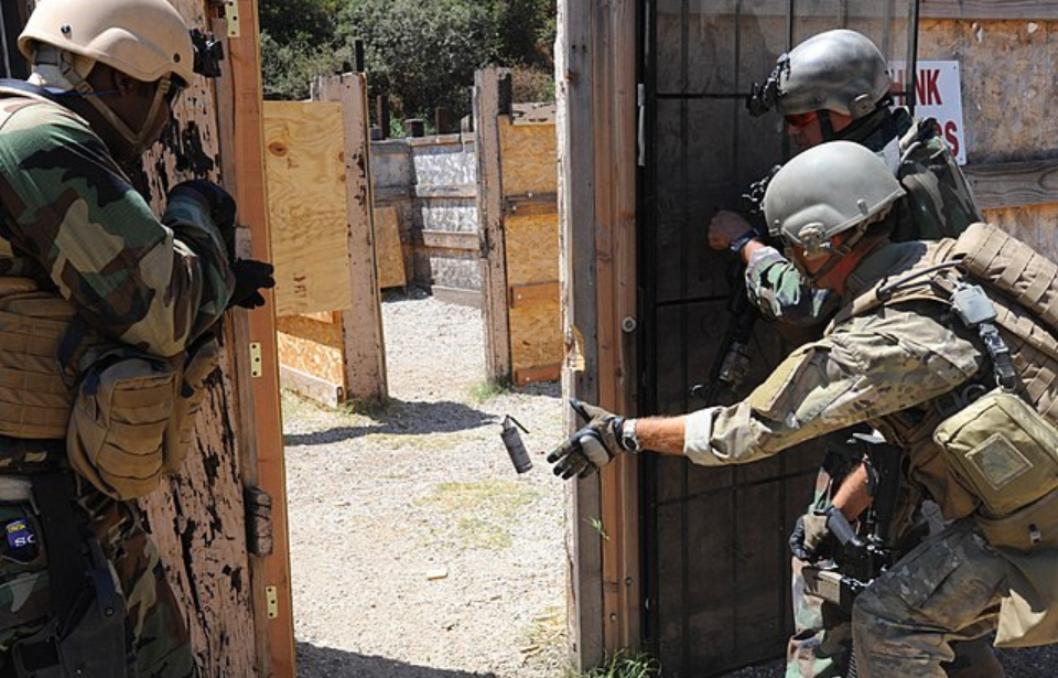 Mass Communication Specialist 1st Class James E. Foehl tosses a flashbang grenade while two other armed servicemen watch