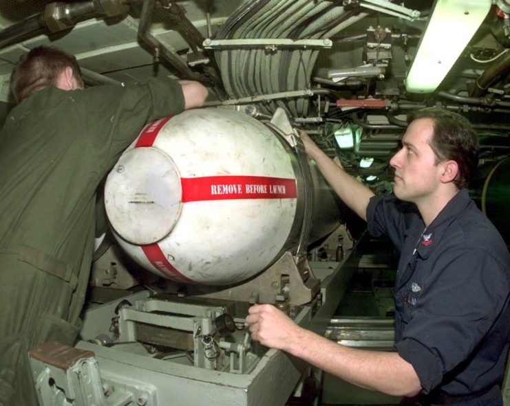 A machinist's mate attaching a Tomahawk missile capsule to the pivot tray in the torpedo room while another sailor watches