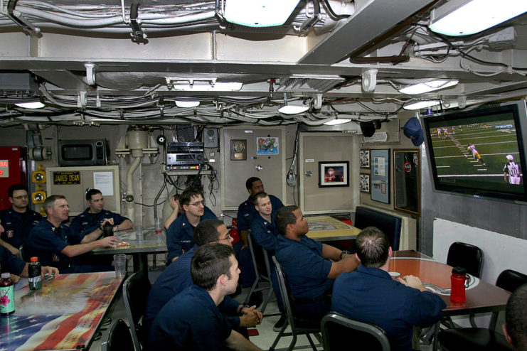 Sailors sitting around lunch tables while watching football on a television