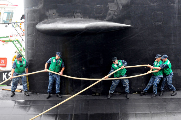 Five US Navy sailors tie off a rope to secure the USS Dallas (SSN-700)