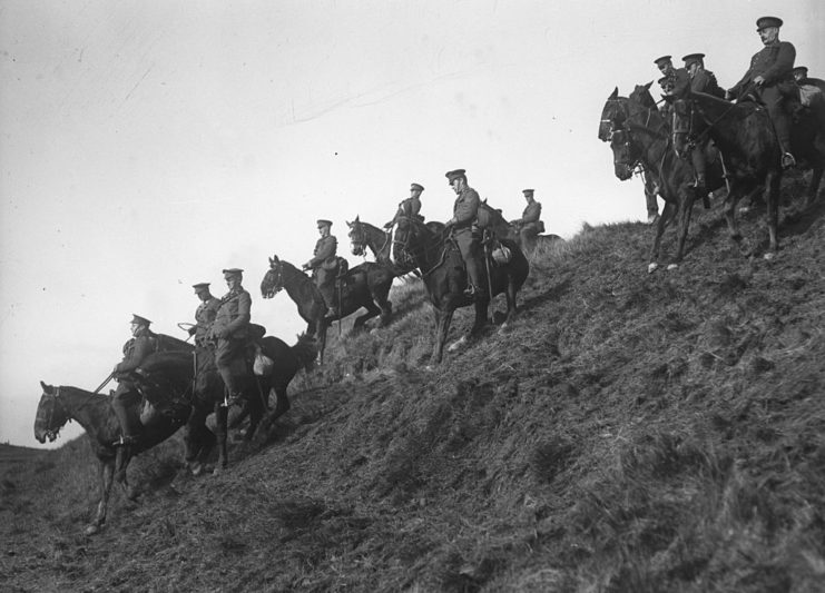 Canadian cavalrymen riding horses down a muddy hill