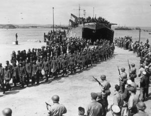 Soldiers standing around prisoners of war walking off of a boat