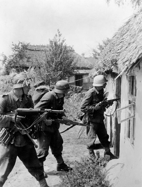 Three German soldiers running into a house while wielding MP 40s