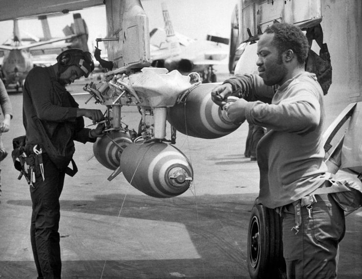 Two US Navy crewmen attaching fuse bombs to the bottom of a McDonnell Douglas F-4 Phantom II