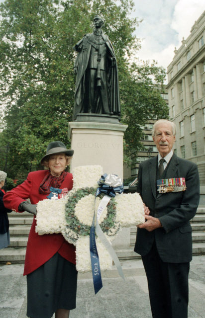 Odette Sansom and Laurence Sinclair holding a cross-shaped wreath in front of the King George IV statue at Carlton Gardens