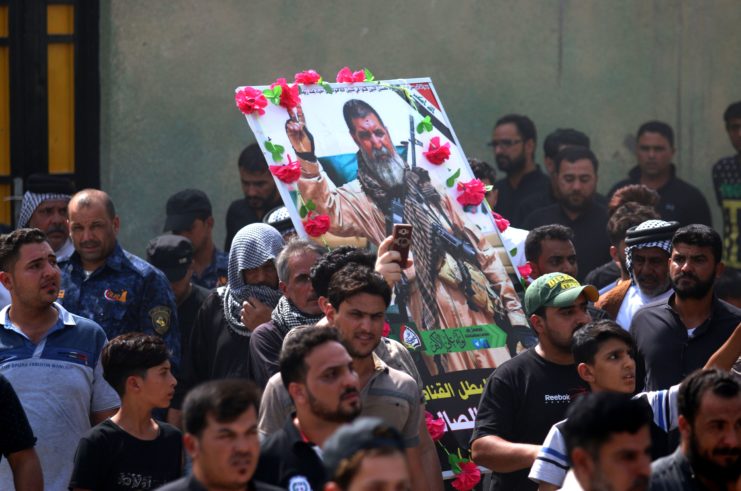 Mourners gathered together, with one holding an image of Abu Tahsin al-Salhi